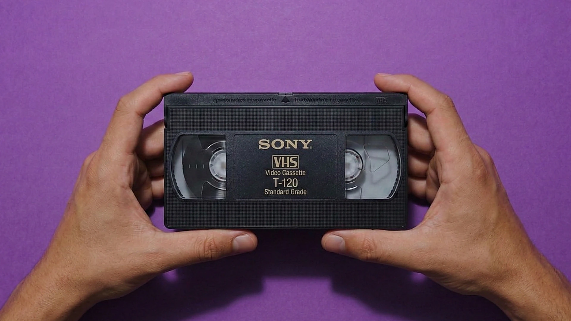 Hands carefully holding a VHS cassette — inspection and gentle handling before repair or transfer