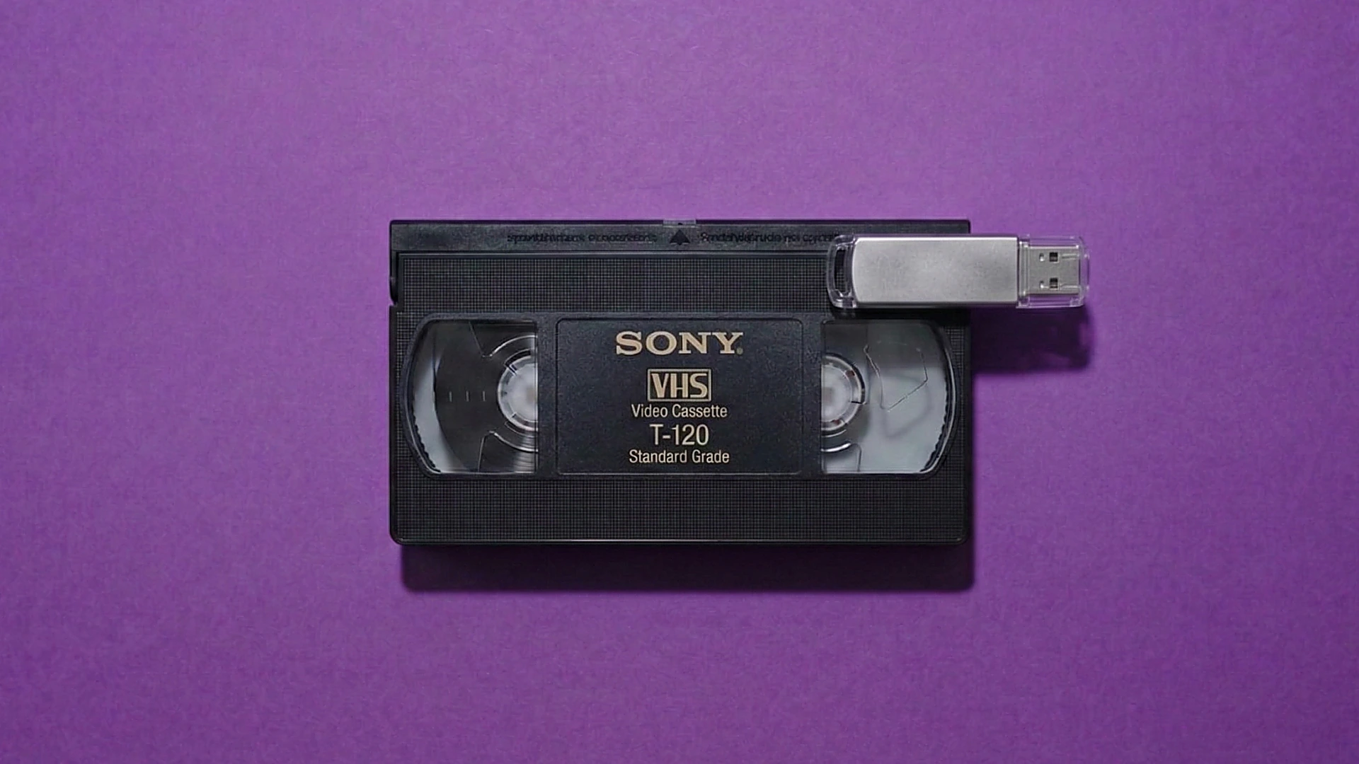VHS cassette beside a USB flash drive — professional transfer to digital files and typical UK pricing context