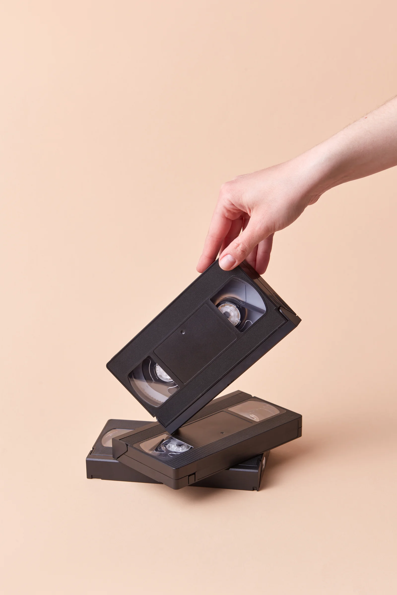 Hand lifting a VHS tape from a tall stack — sorting what to digitise, donate, sell or recycle