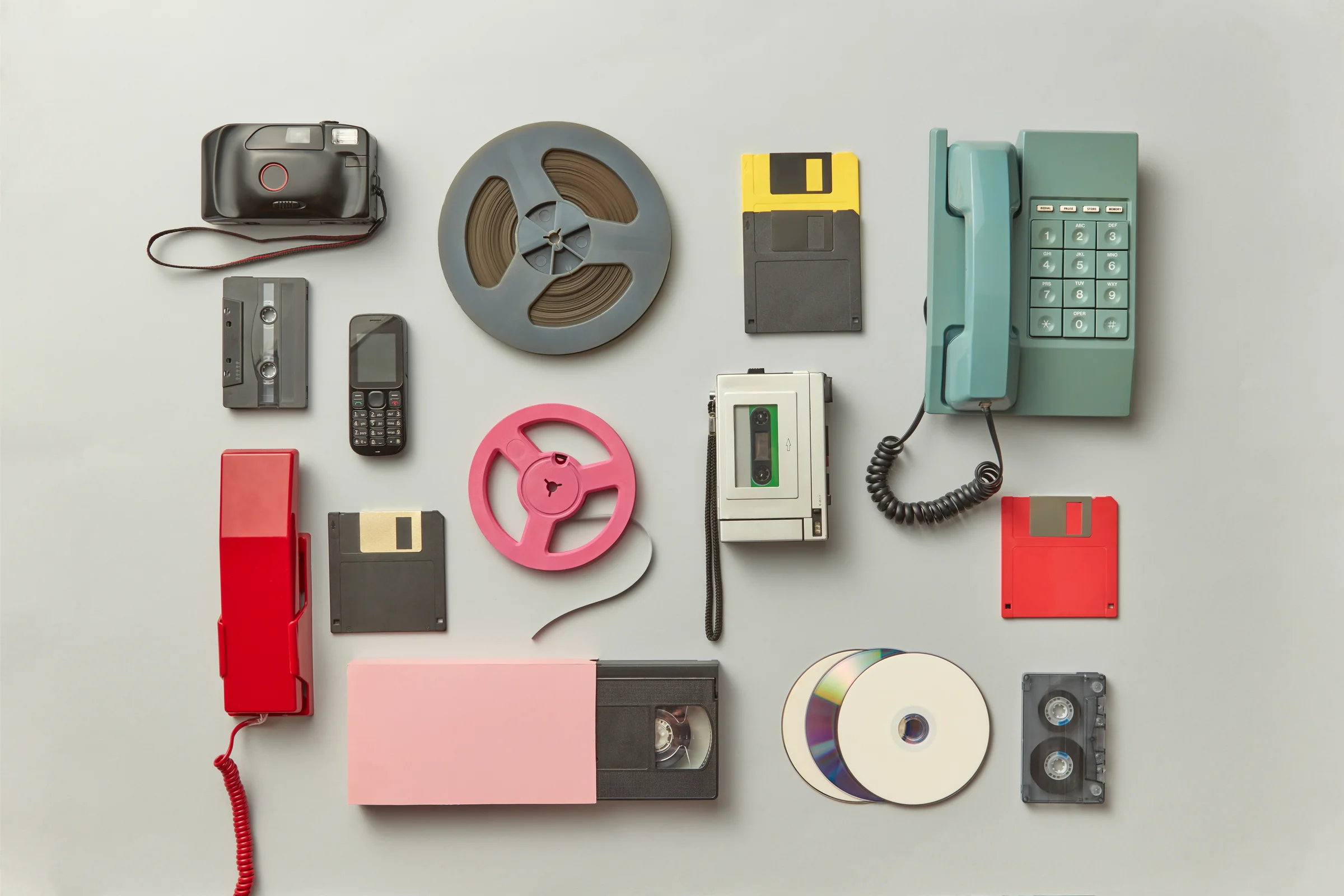 Collection of vintage media formats including VHS tapes, cassettes, film reels, floppy disks and cameras
