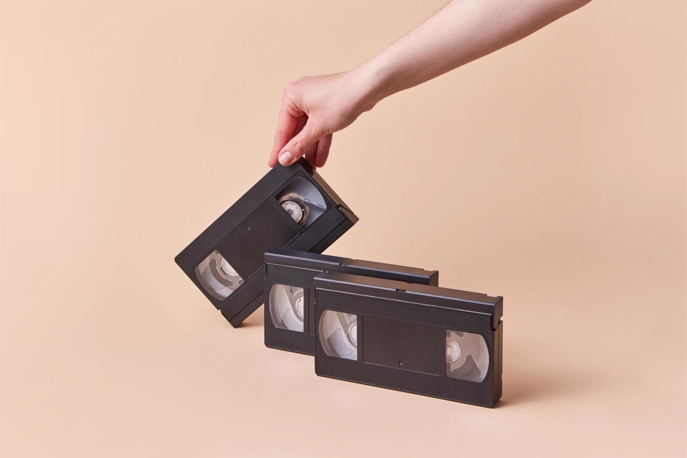 Hand fanning three VHS cassettes — counting and preparing tapes before boxing for tracked UK post