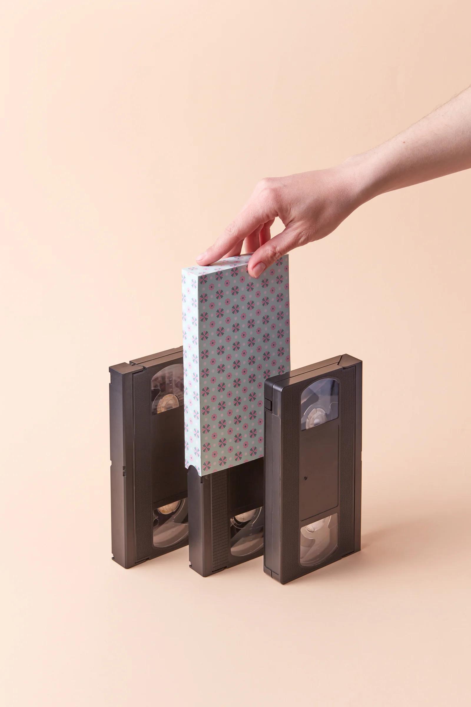 Hand choosing a VHS cassette from a shelf — deciding whether to digitise old recordings