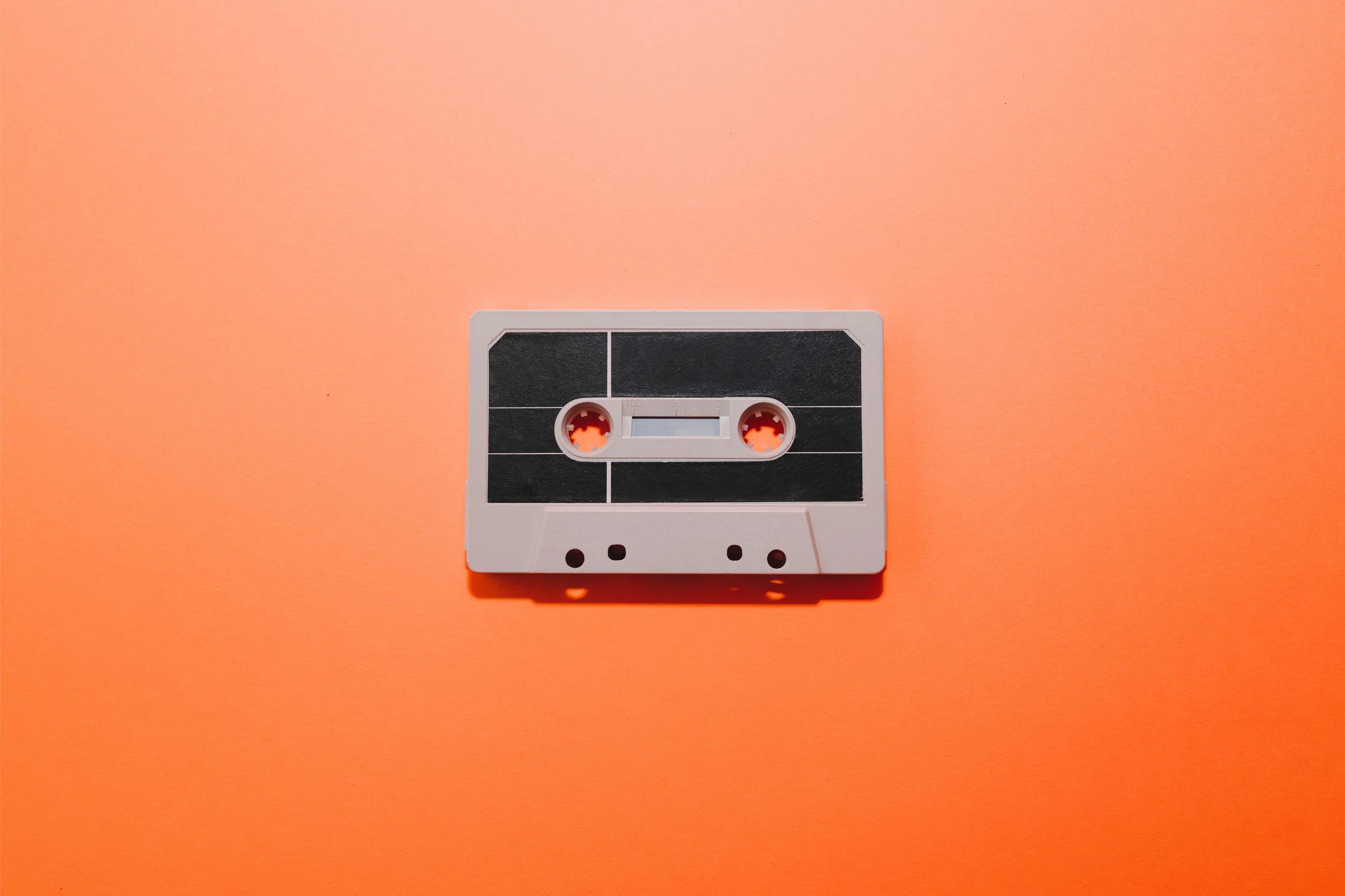 A grey audio cassette with a black label lying on an orange background