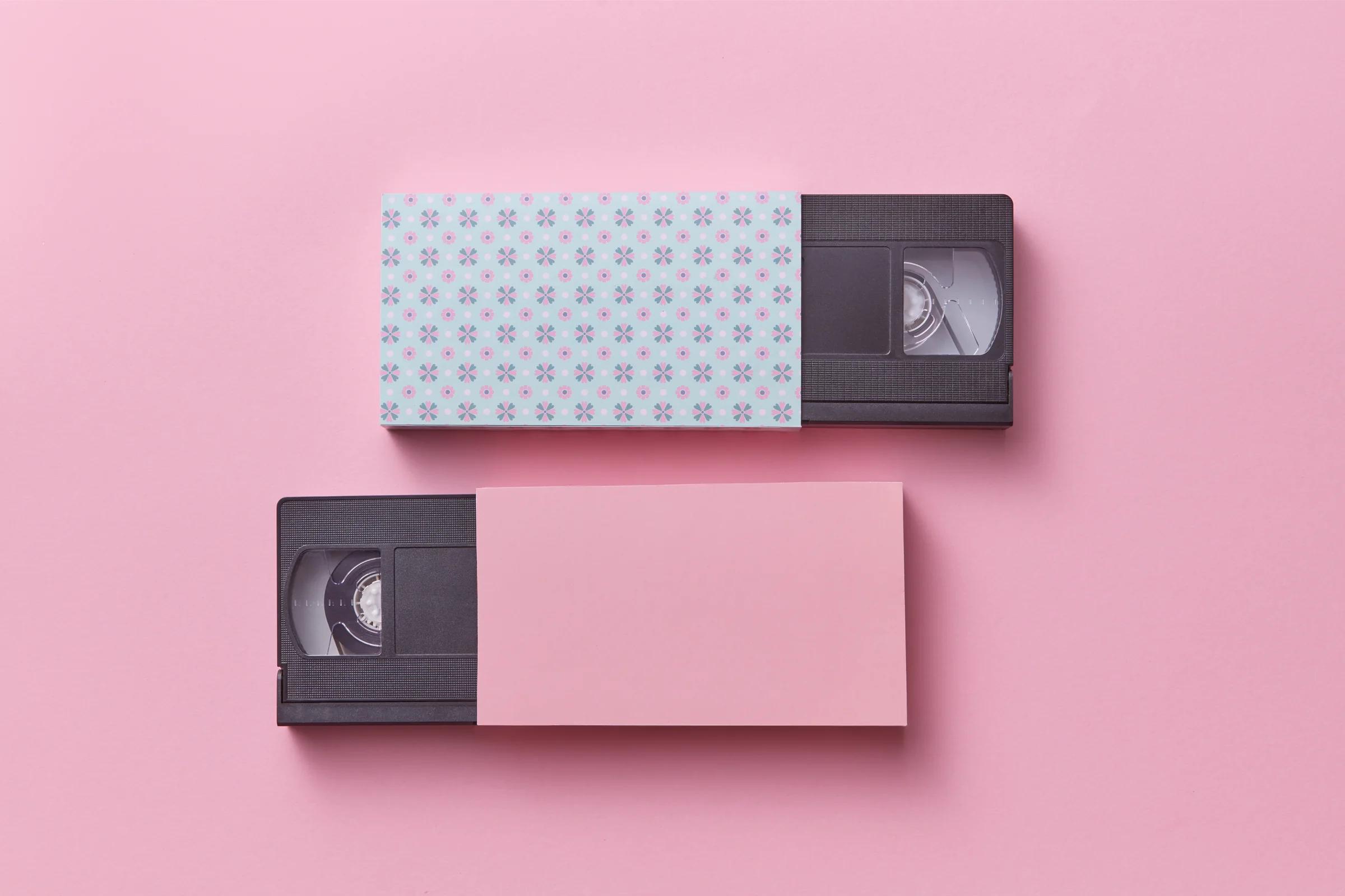 Two VHS tapes half inside patterned paper sleeves on a pink background